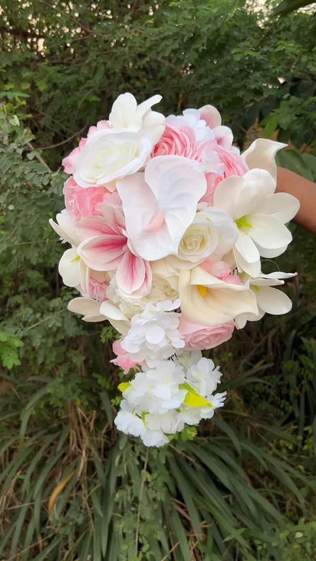 Cascading wedding bouquet with pink and white artificial roses and orchids against greenery.