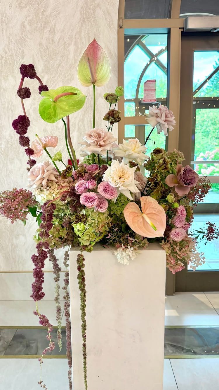 Floral arrangement with pink roses and anthuriums on a white pedestal vase.