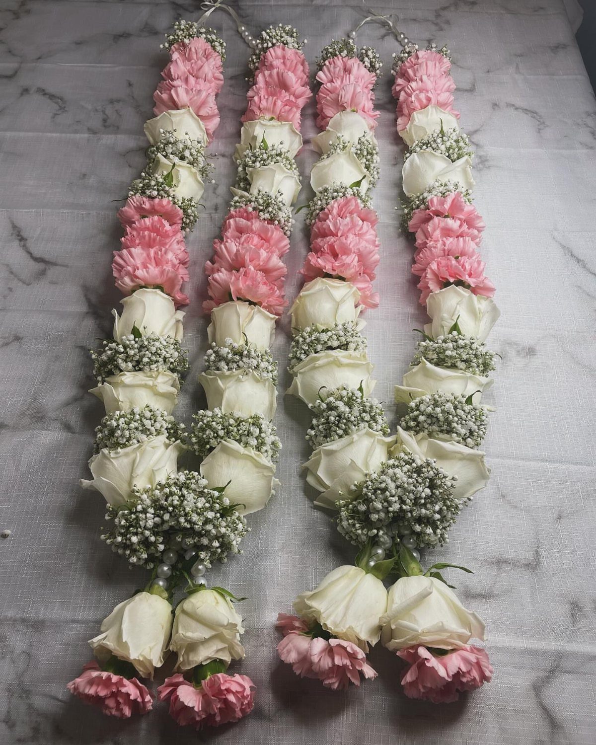 Two floral garlands with pink carnations, white roses, and baby's breath on marble.