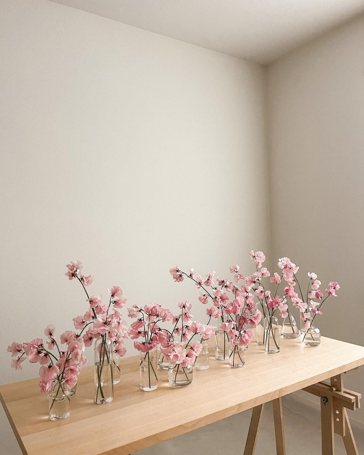 Pink cherry blossom branches in small glass vases on a wooden table.