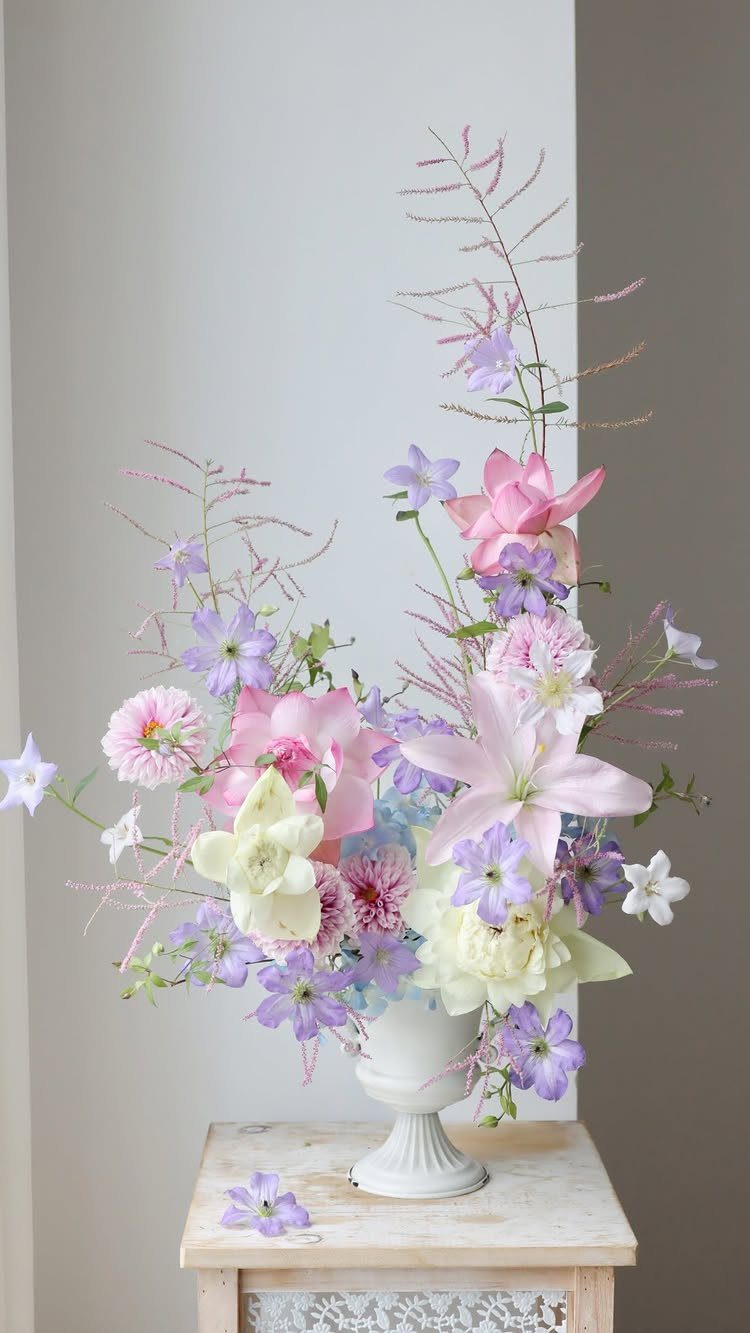 Pink lilies and purple flowers in a white vase on a wooden table