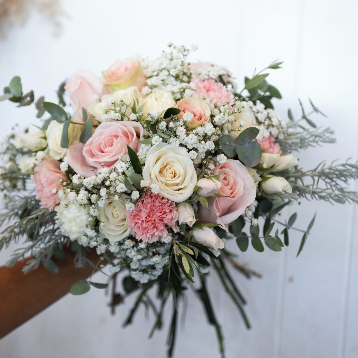 Bridal bouquet with pink roses, carnations, and baby's breath against white wood.