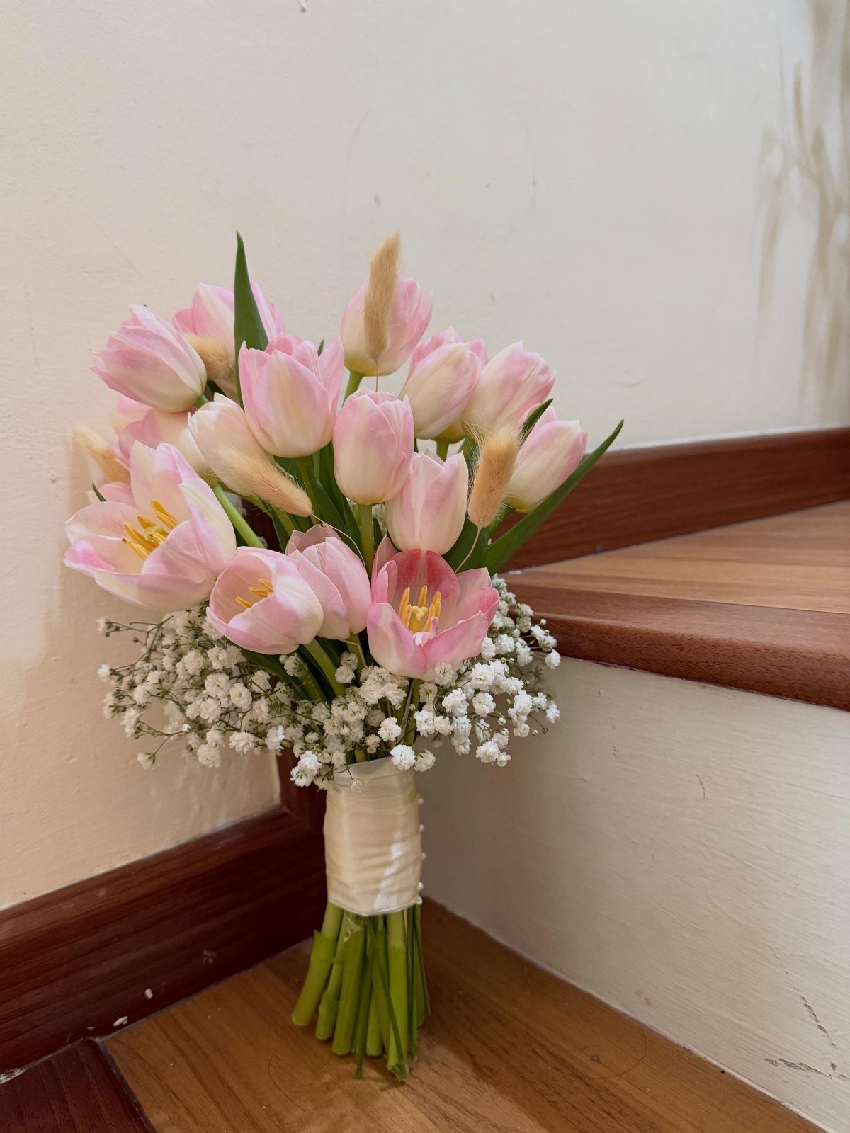 Pink tulip bridal bouquet with baby's breath resting on wooden stairs