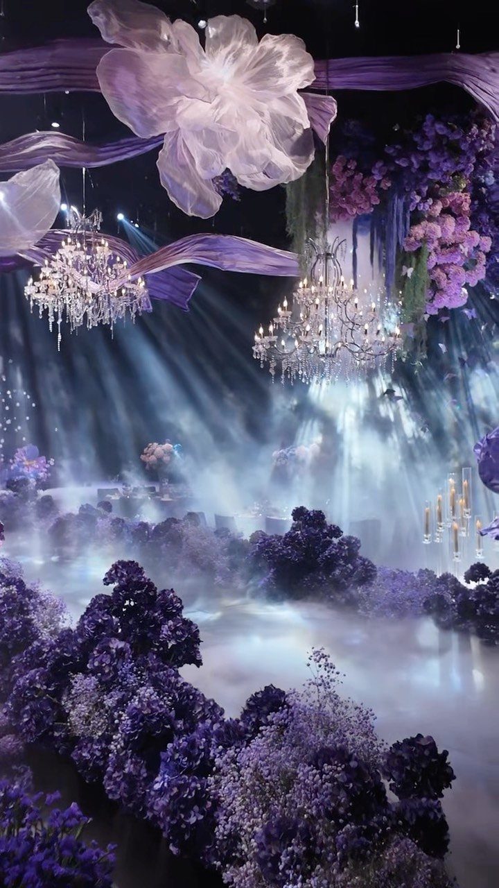 Opulent event space with purple flowers, crystal chandeliers, and ethereal fog and lighting.