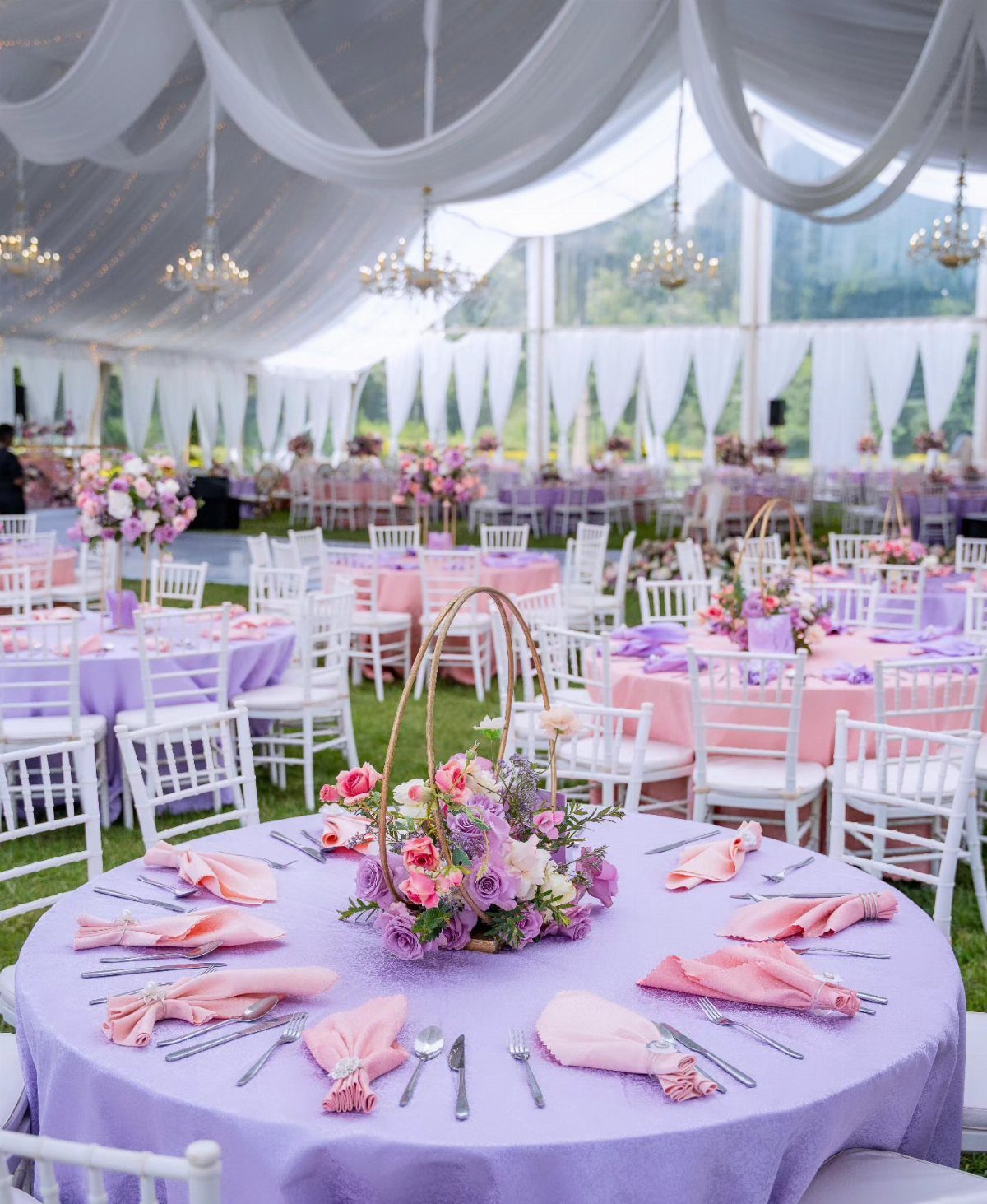 Purple and pink floral centerpieces on tables with purple cloths in a tent.