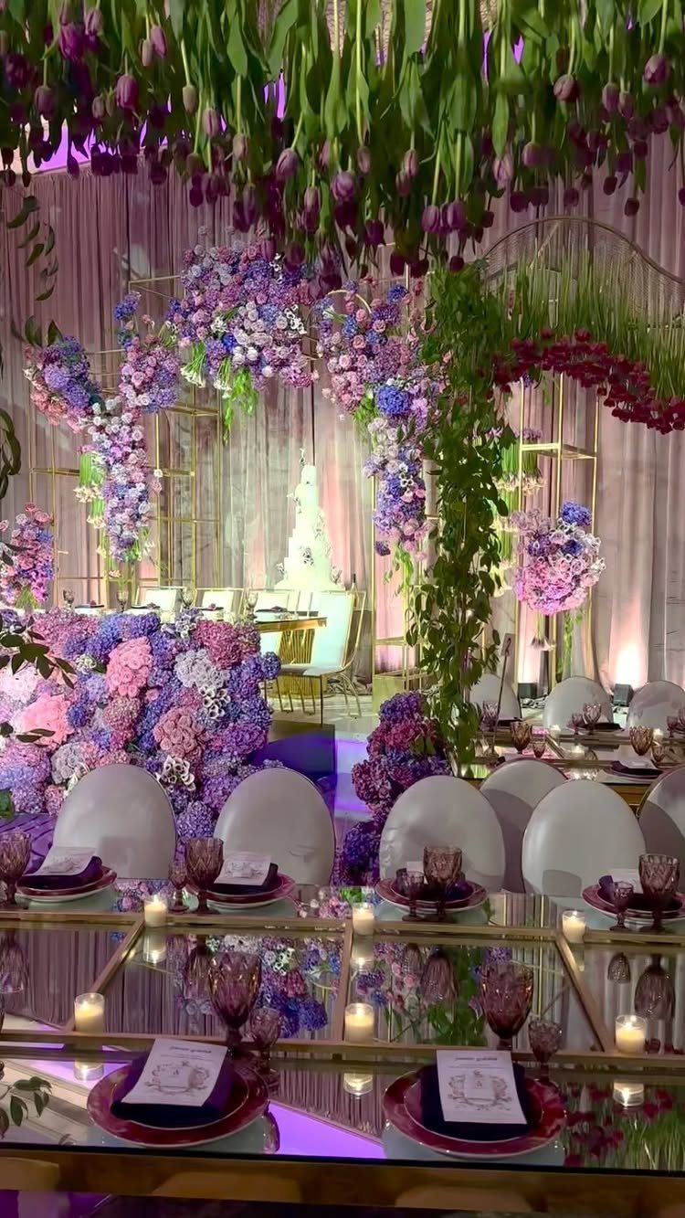 Purple floral arches and hanging green foliage over mirrored wedding reception tables.