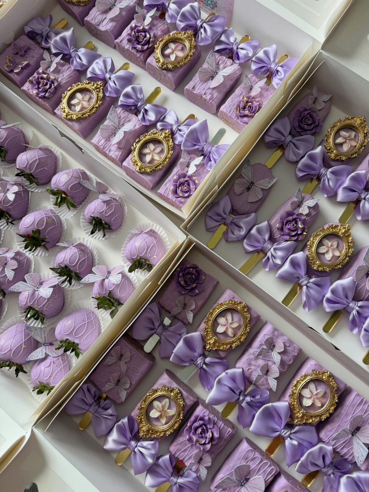 Purple chocolate-covered strawberries and cake pops with lilac ribbons in white boxes.