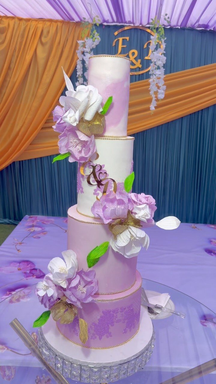 Four-tier purple and white wedding cake with sugar flowers on a crystal stand.