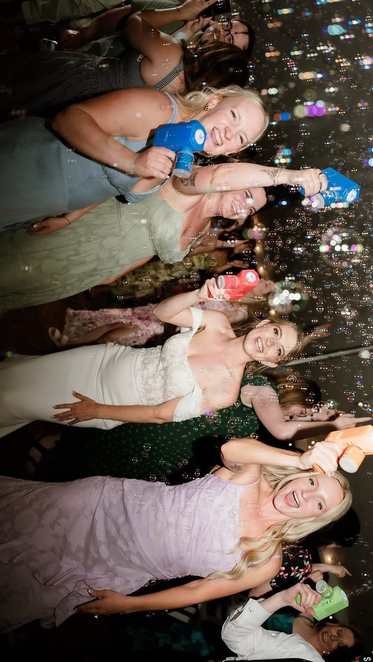 Women in formal dresses using bubble machines to create bubbles at a wedding.