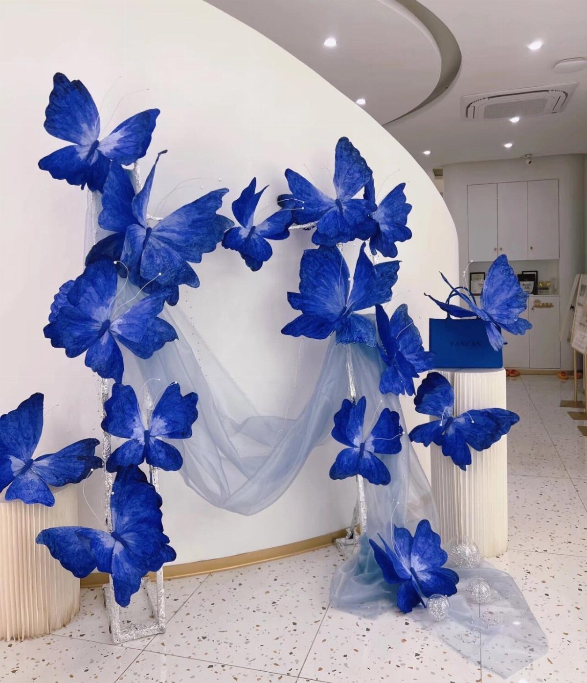 Large blue decorative butterflies arranged on a white wall with sheer blue fabric.