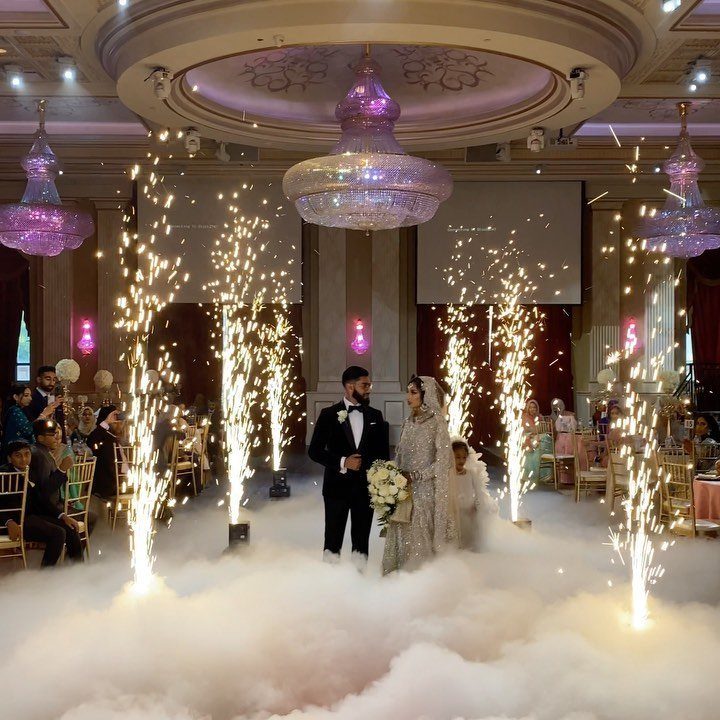 Bride and groom walking through fog with sparklers in a grand ballroom