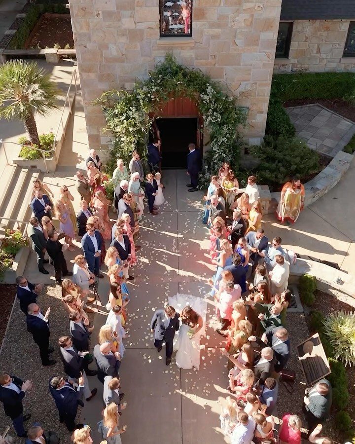 Bride and groom walking through a confetti shower exiting a stone church