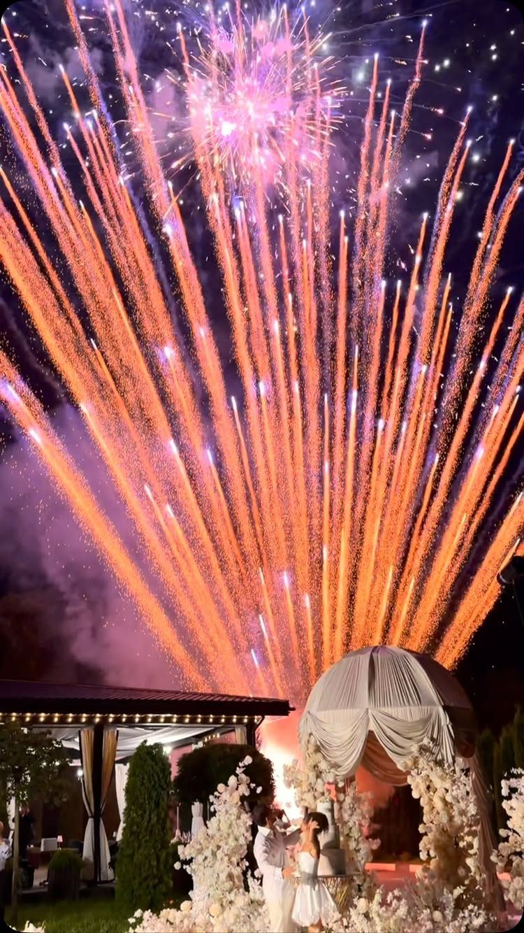 Couple under a white gazebo with large orange and purple fireworks exploding above
