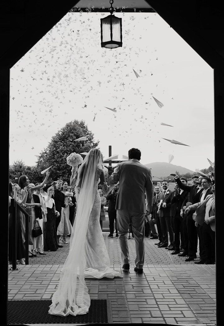 Bride and groom walking through guests throwing white paper airplanes during a wedding exit.
