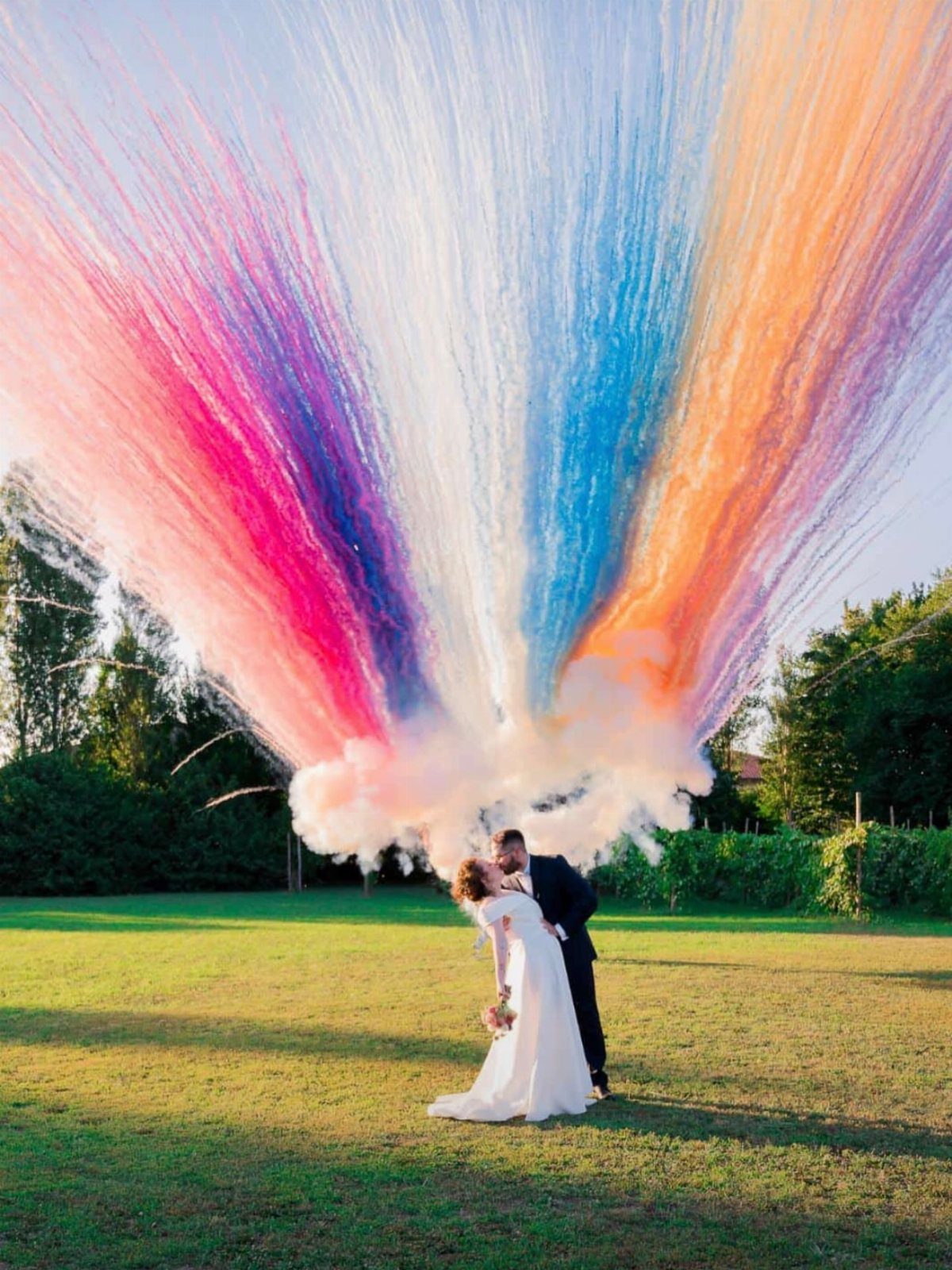 Bride and groom kissing under a large burst of colorful smoke in a field