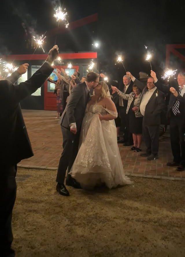 Bride and groom kissing while guests hold lit sparklers during a night exit.