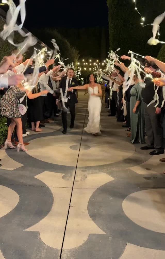 Bride and groom walking through a guest tunnel waving white ribbon streamers