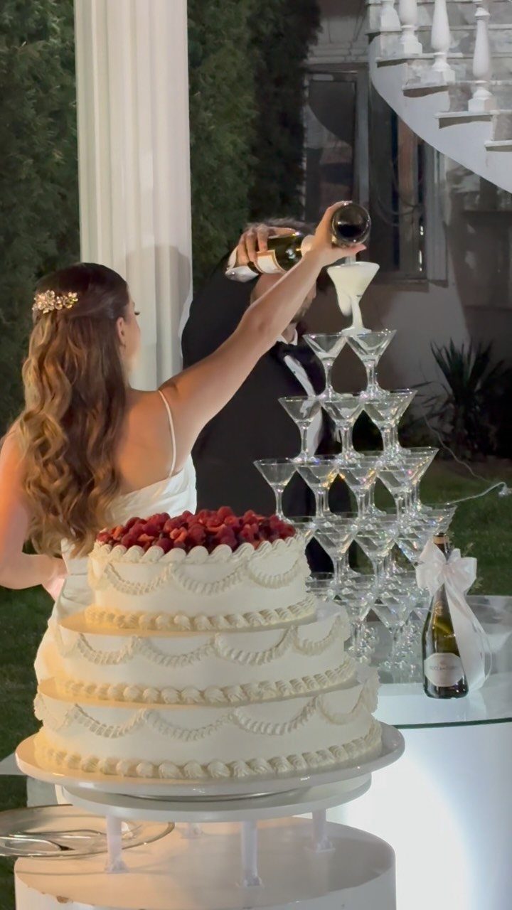 Bride and groom pouring champagne into a tiered glass tower next to a cake