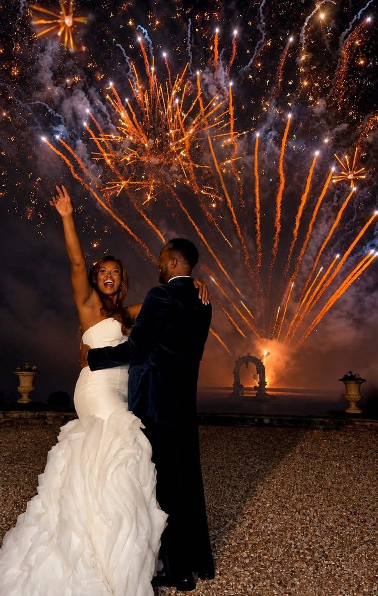 Bride and groom embracing under a grand display of orange wedding fireworks.