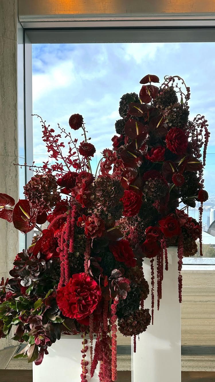 Deep red floral arrangements atop two tall white cylindrical pedestals by a window.