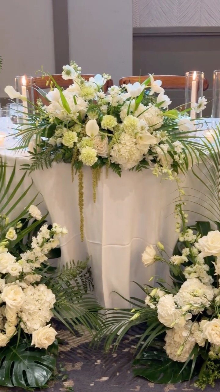 Small wedding table with white floral arrangements and lit cylinder candles.