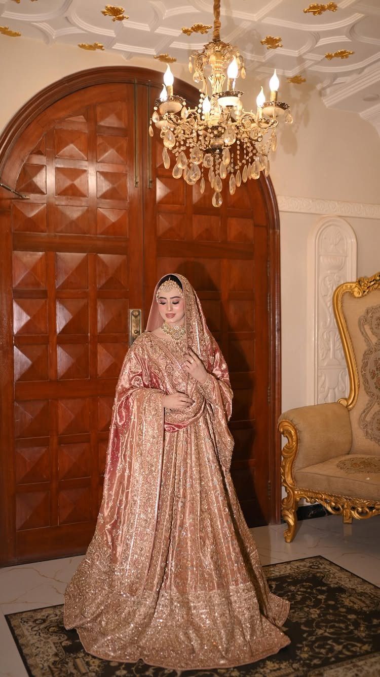 Woman in a shimmering rose gold bridal gown standing under a crystal chandelier.