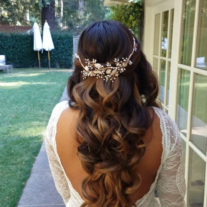 Woman with curly hair wearing a rose gold floral hairpiece and lace dress.