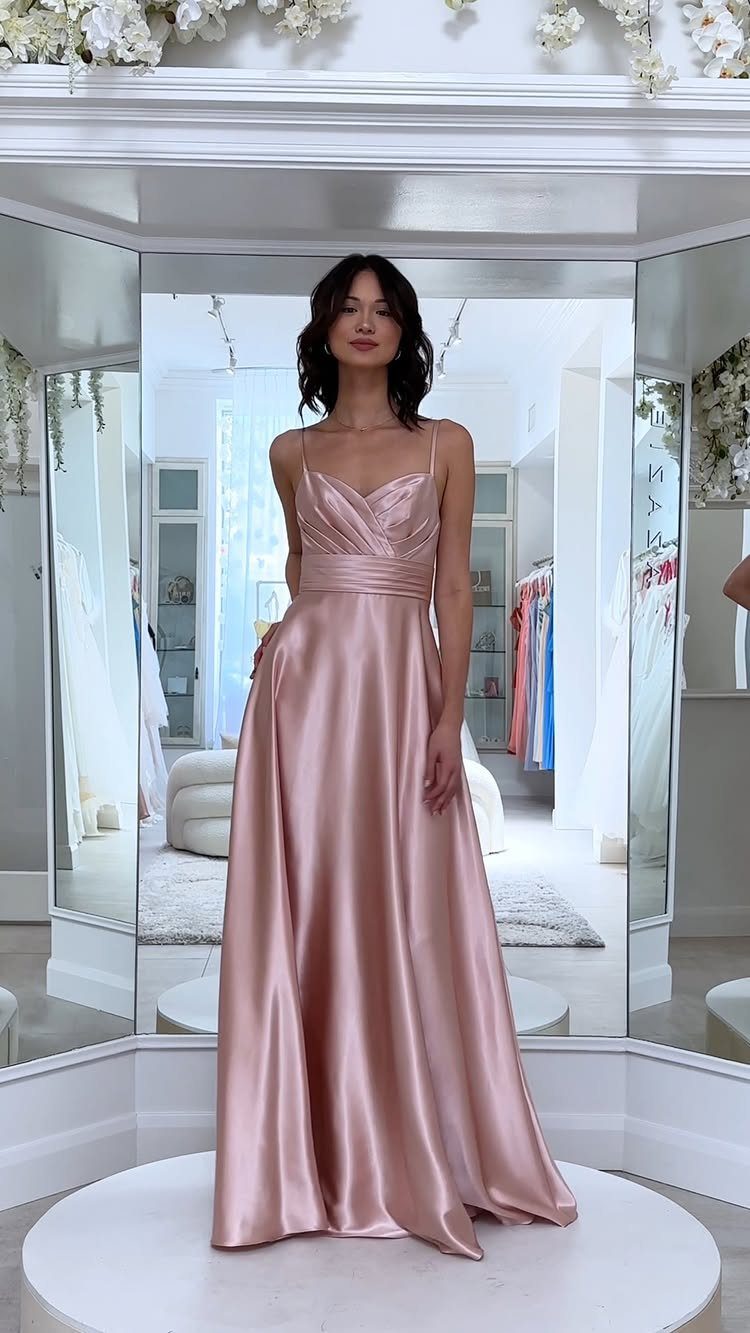 Woman wearing a long rose gold satin gown in a bright bridal boutique.