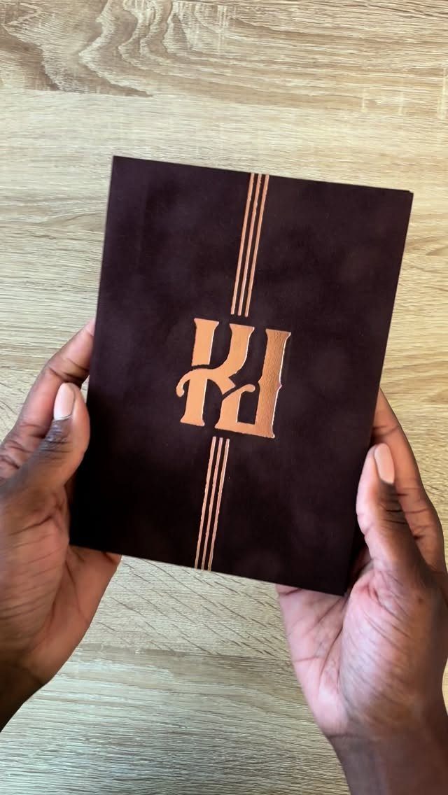 Rose gold foil initials on a burgundy velvet wedding guest book held by hands