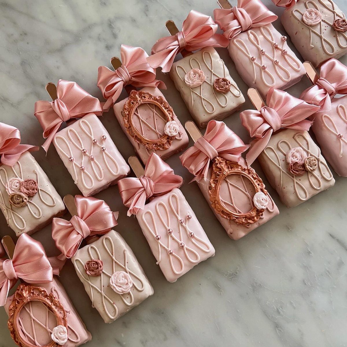 Rose gold cake pops with pink satin bows on a marble background