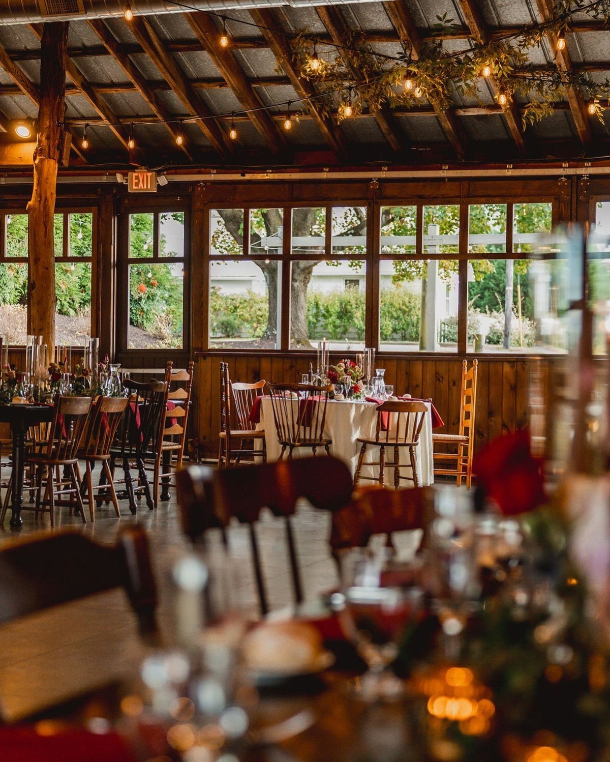 Barn reception space with wooden beams, string lights, and set dining tables.