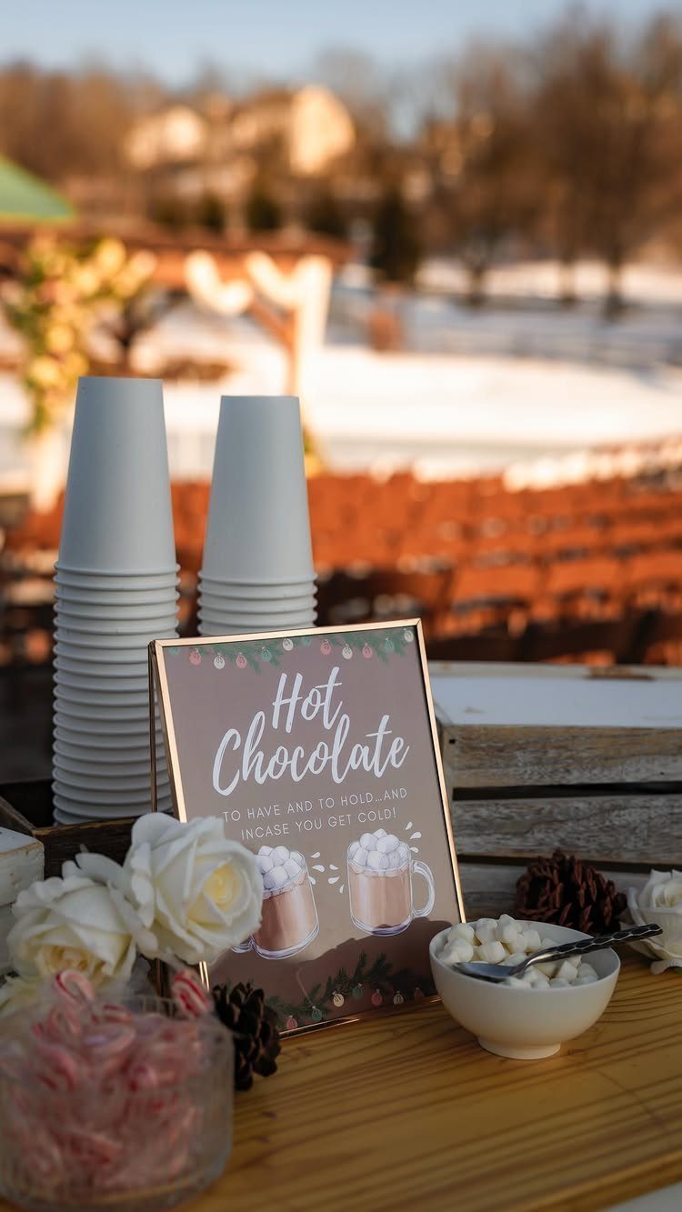 Hot chocolate station with white cups and marshmallows in a snowy outdoor setting
