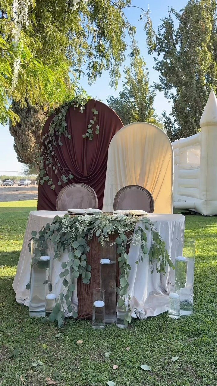 Sweetheart table decorated with cascading eucalyptus greenery and floating candles outdoors.