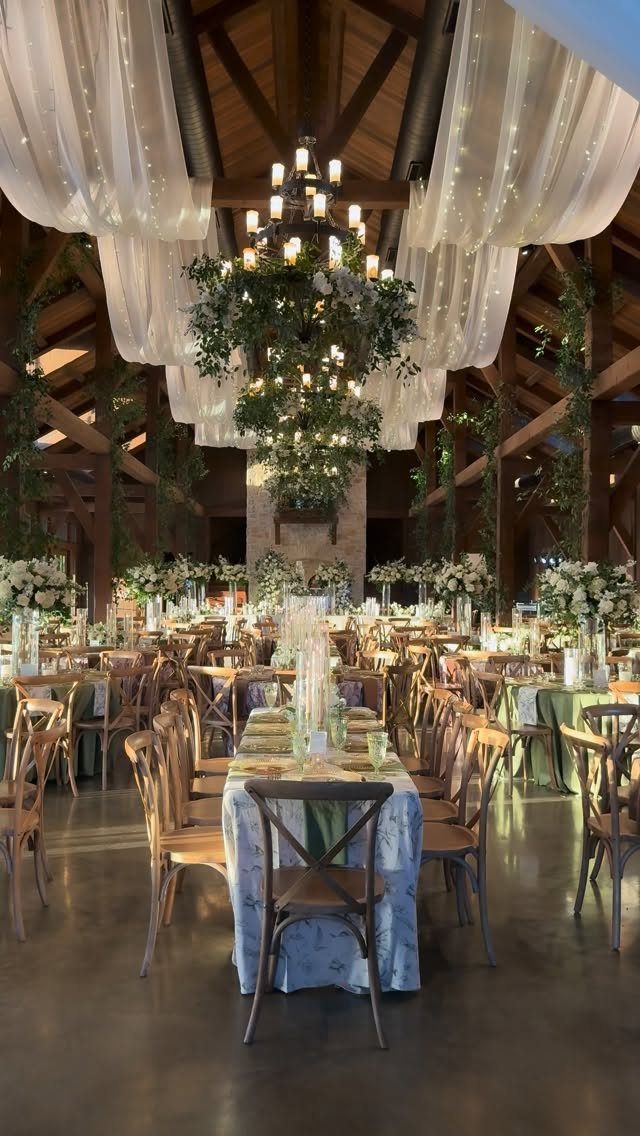 Barn wedding venue with wooden beams, white fabric draping, and long decorated tables.
