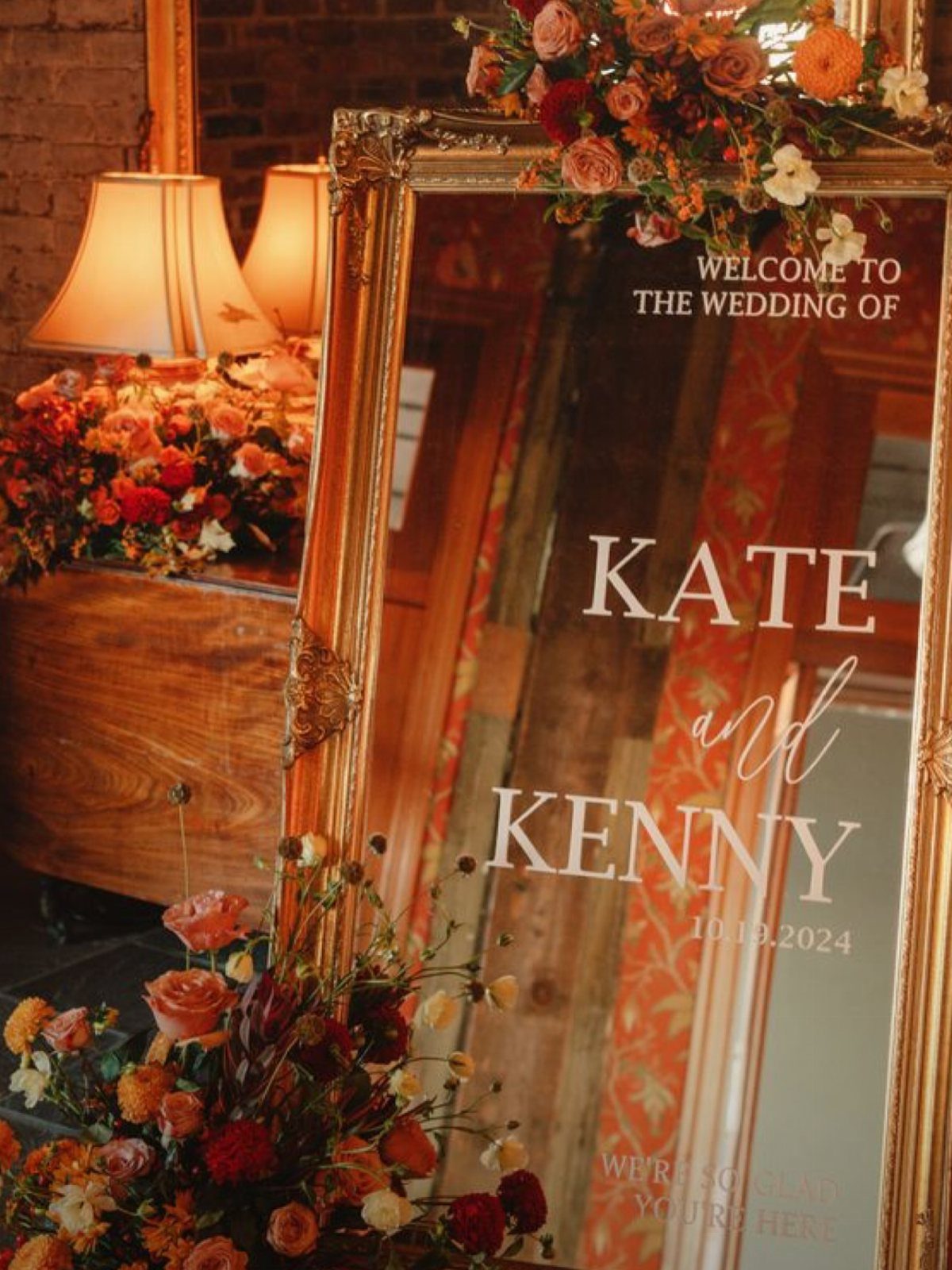 Gold-framed mirror wedding sign decorated with autumn orange and red floral arrangements.