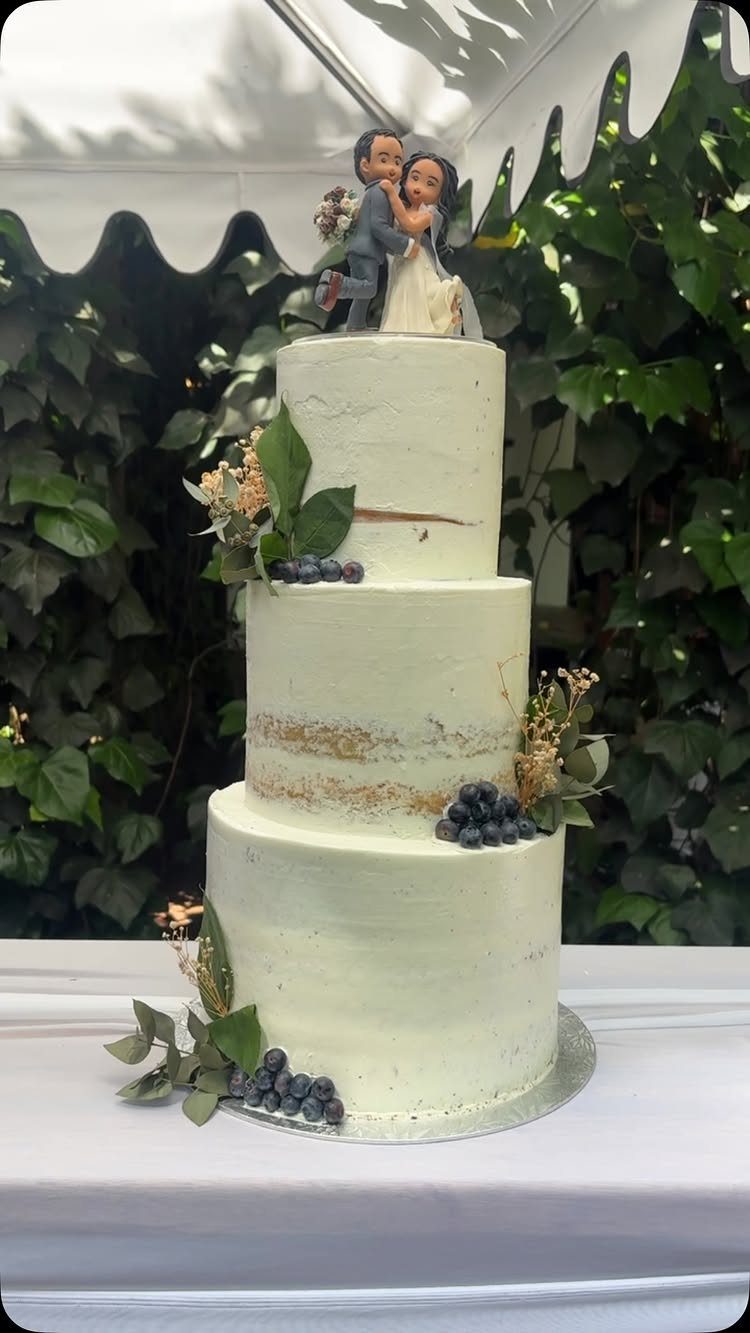 Three-tiered semi naked wedding cake decorated with blueberries and greenery and a topper.