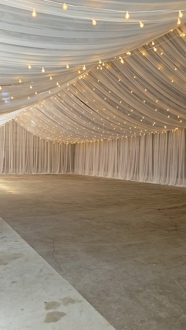 White fabric ceiling draping with warm string lights in an empty event space