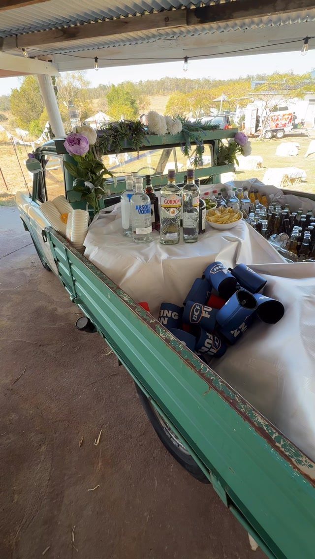 Green vintage farm truck bed used as a rustic beverage station with floral accents.