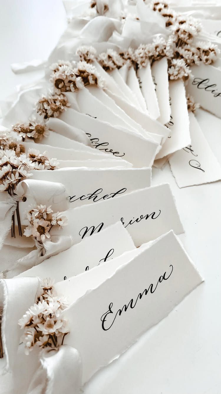 Hand-torn white paper escort cards with calligraphy and dried white flowers.