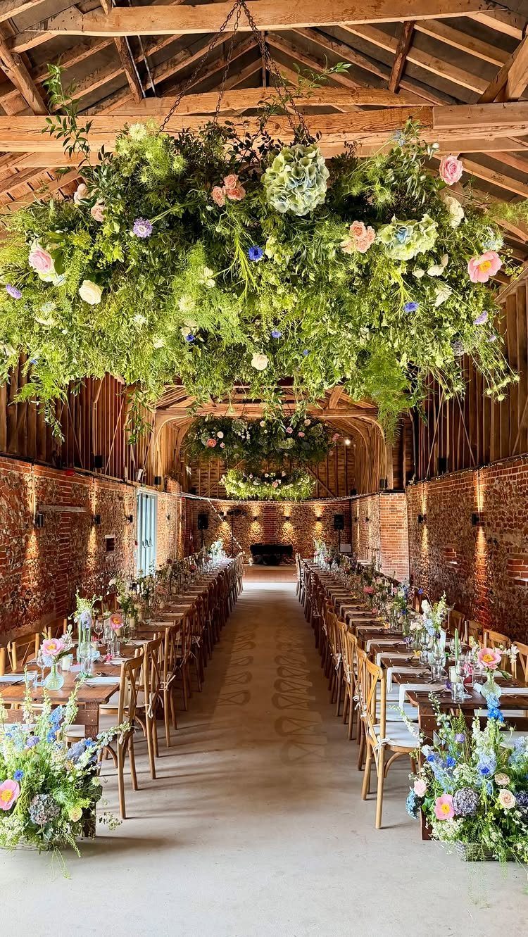 Floral installations hanging from wooden beams over long wedding tables in a barn.