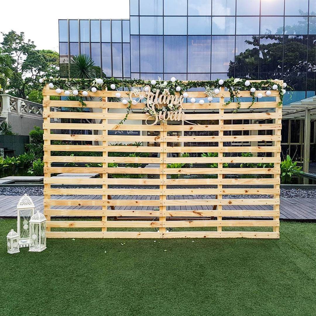 Wooden pallet wall backdrop decorated with white flowers and gold script signage outdoors