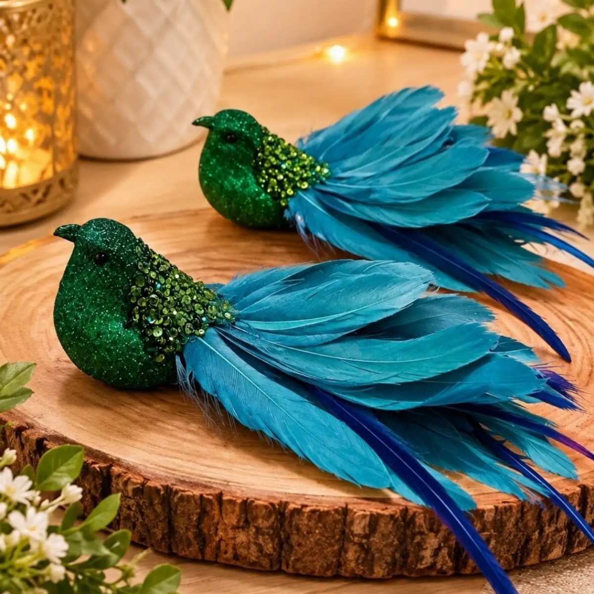 Two glittery green and blue feather birds on a rustic wooden log slice.
