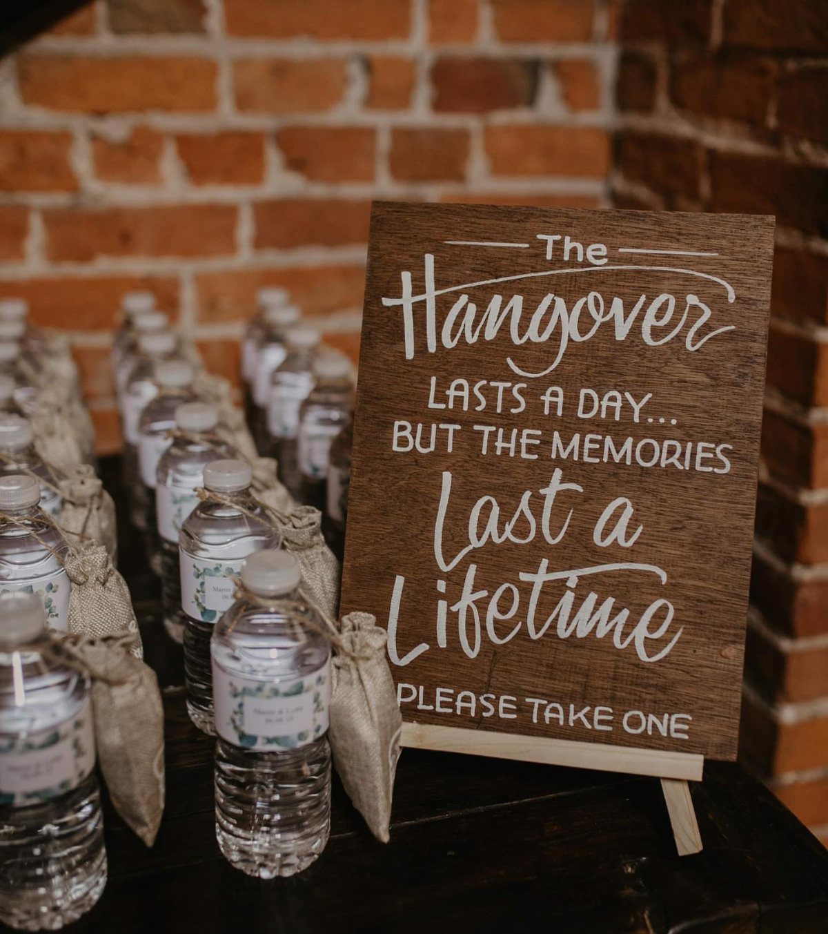 Wooden sign with white calligraphy next to water bottles in burlap sleeves.