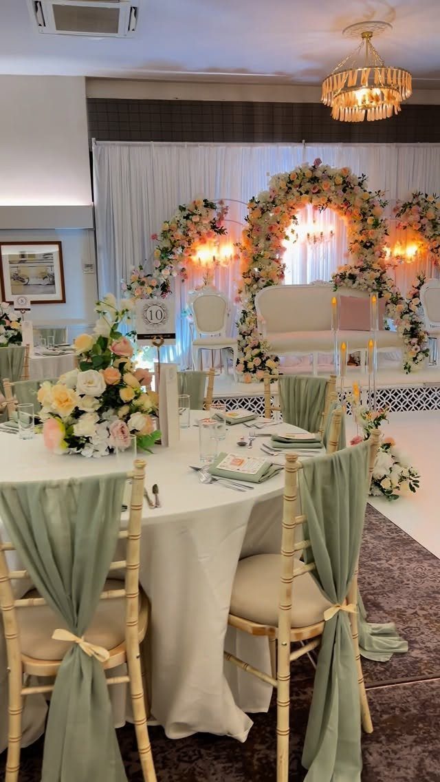 Wedding reception with sage green chair sashes and blush pink floral arrangements.