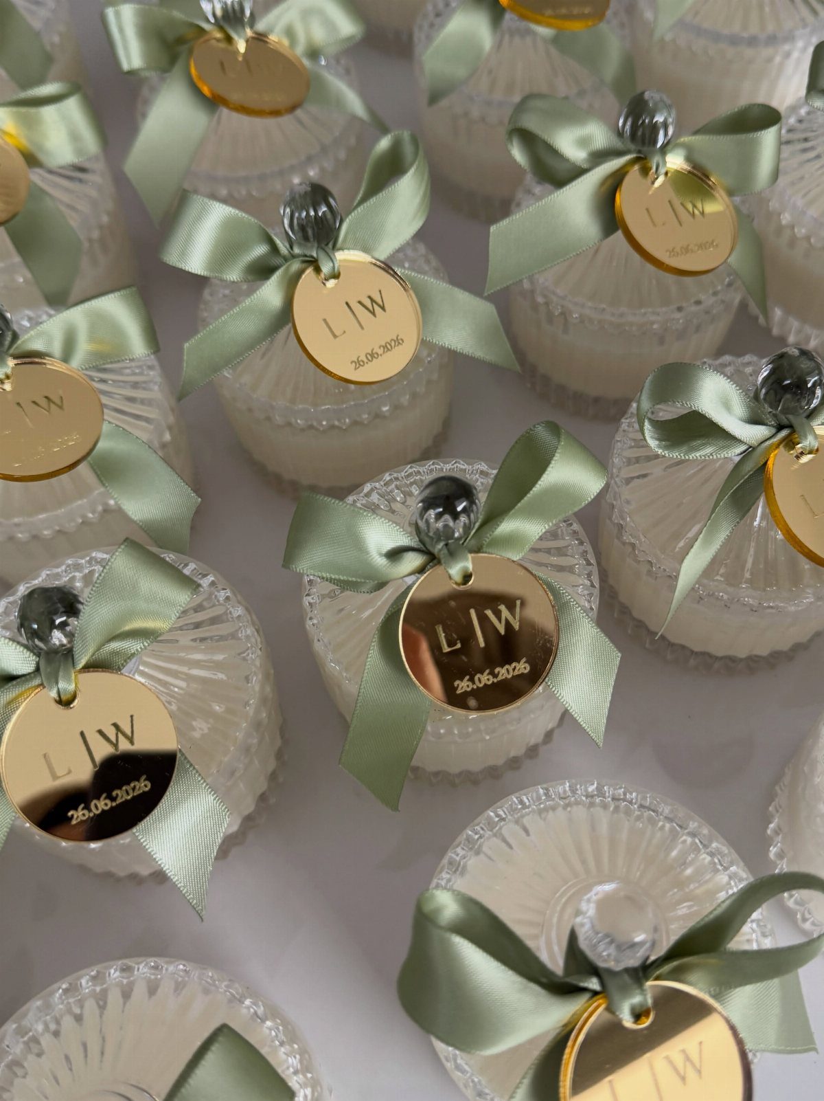 White candles in glass jars with sage green ribbons and gold personalized tags.