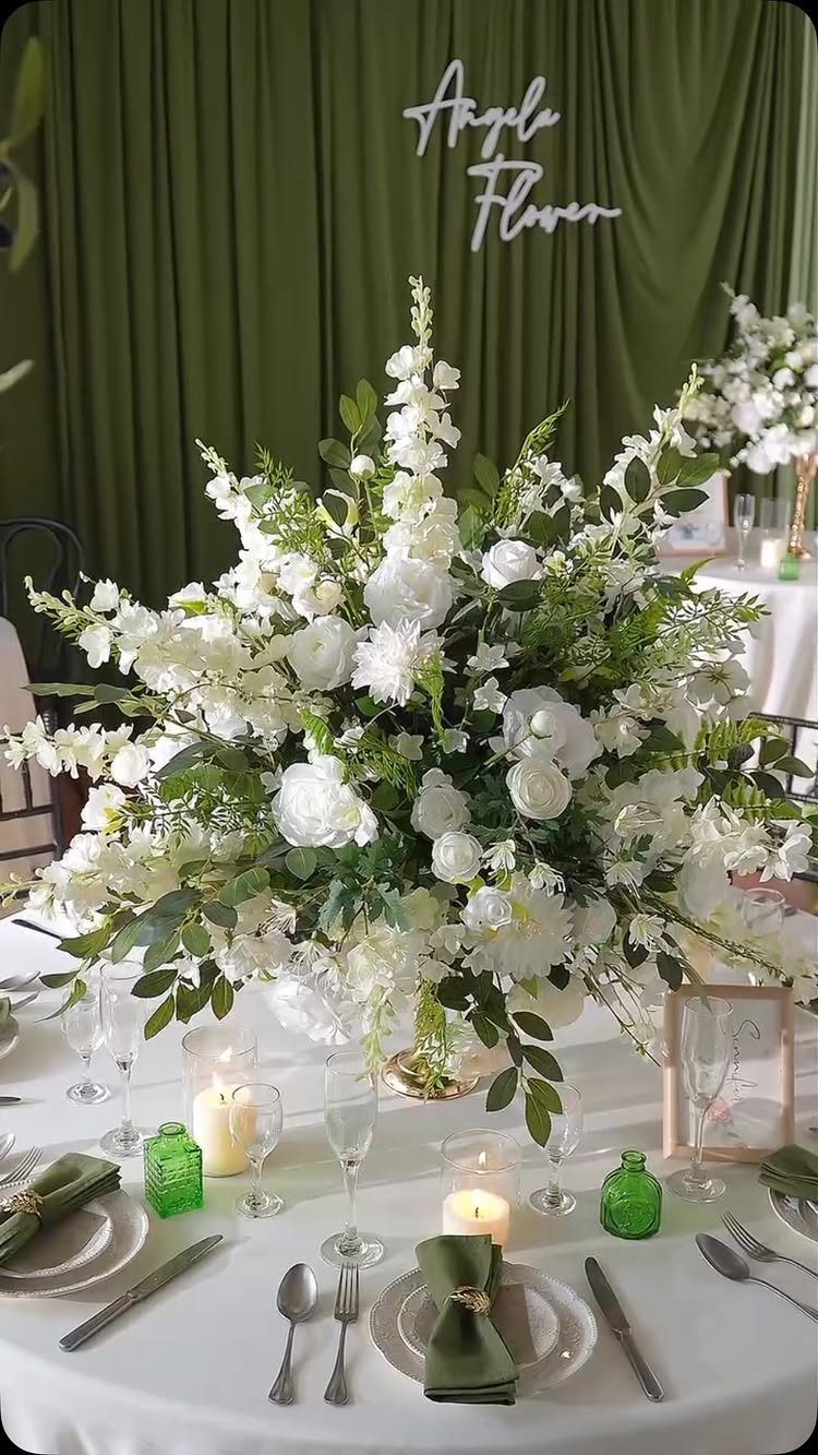 White rose and greenery floral arrangement on a wedding table with sage green accents.