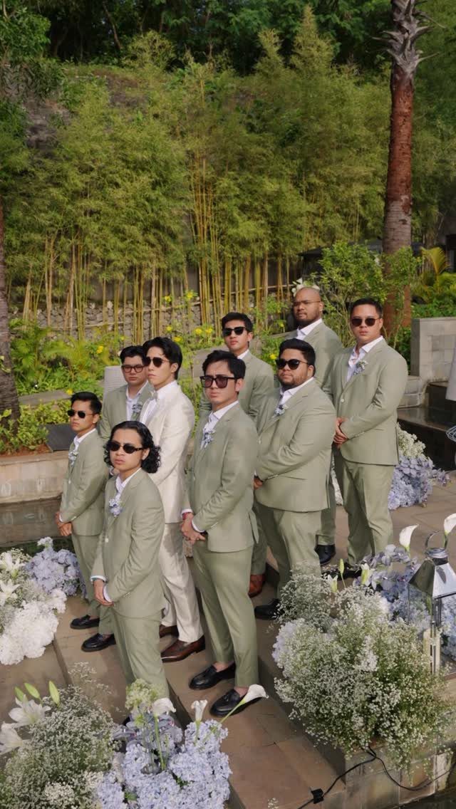 Men and a boy in sage green suits posing outdoors with bamboo background.