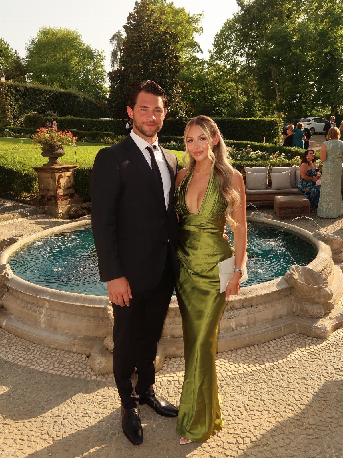 Woman in a sage green satin dress and man in a black suit posing.