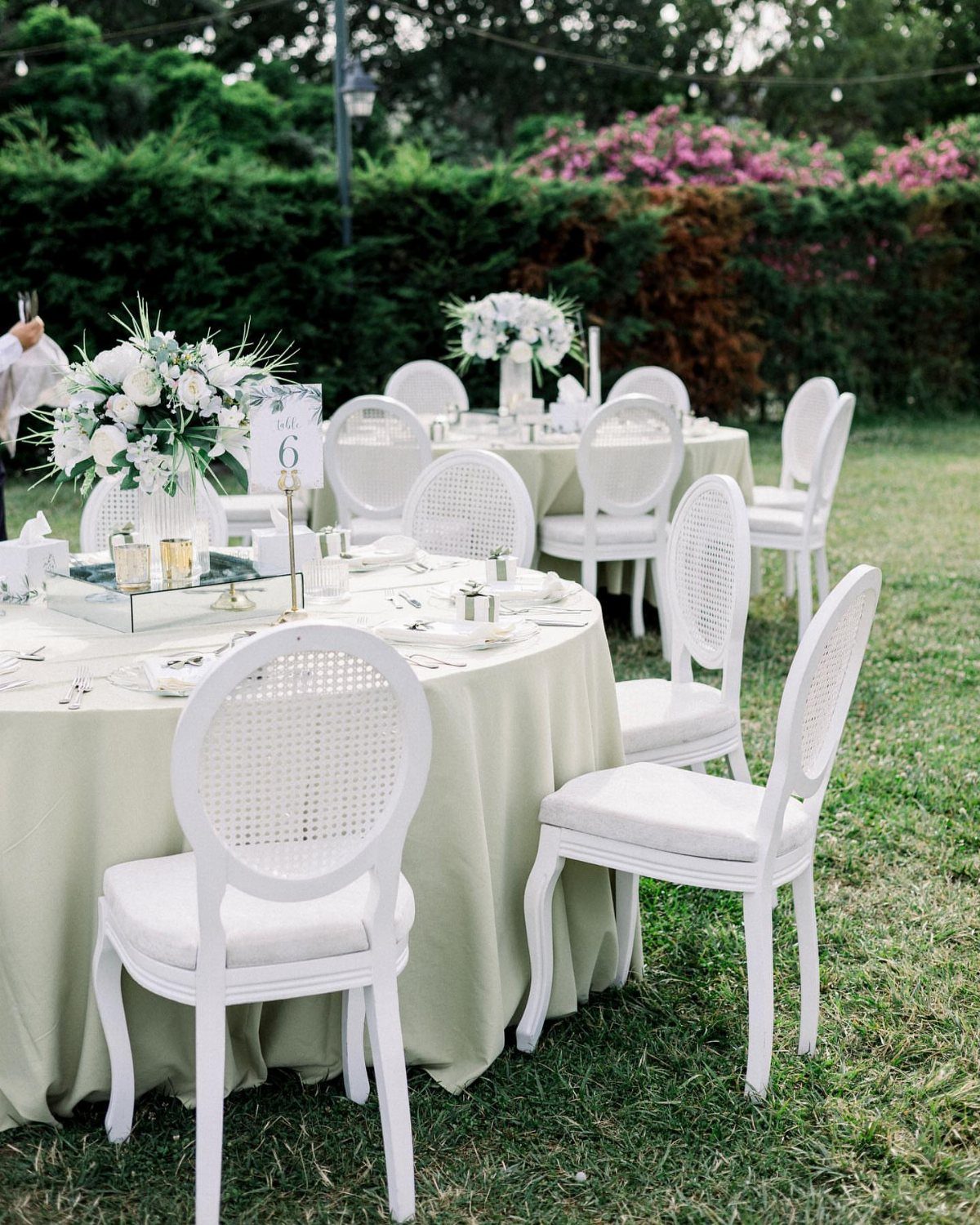 Sage green table linens and white chairs with white floral centerpieces outdoors.