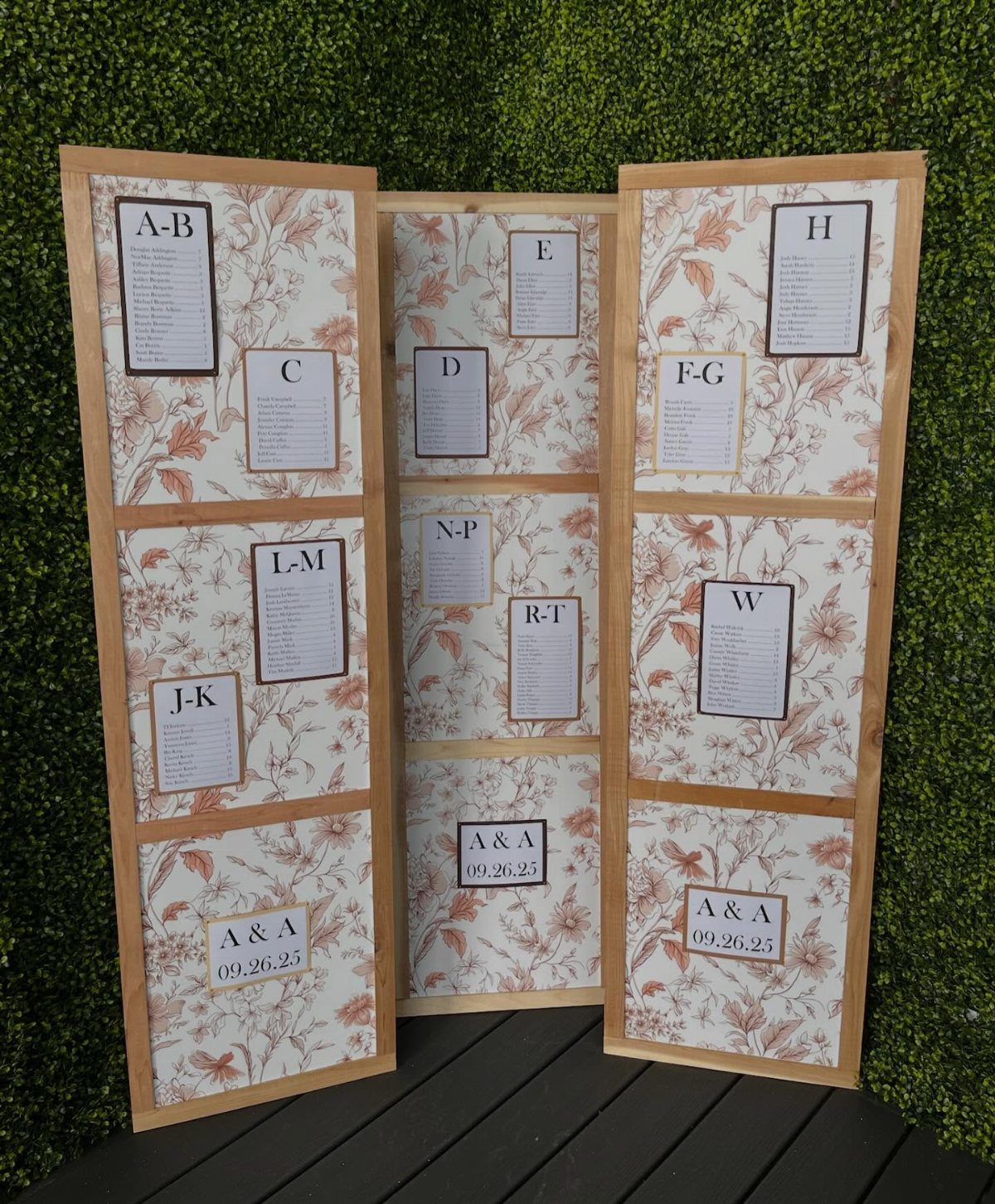 Wooden folding screen with alphabetical guest lists against a green hedge background